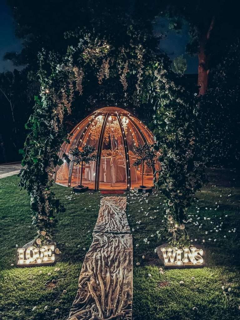 Fairylit dome with floral arch for proposal with light up letters saying Love Wins